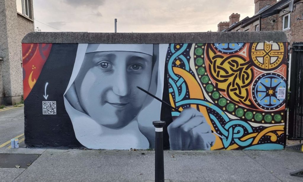 Colorful street mural depicting a nun, adorned with Celtic patterns and a visible QR code for more details.