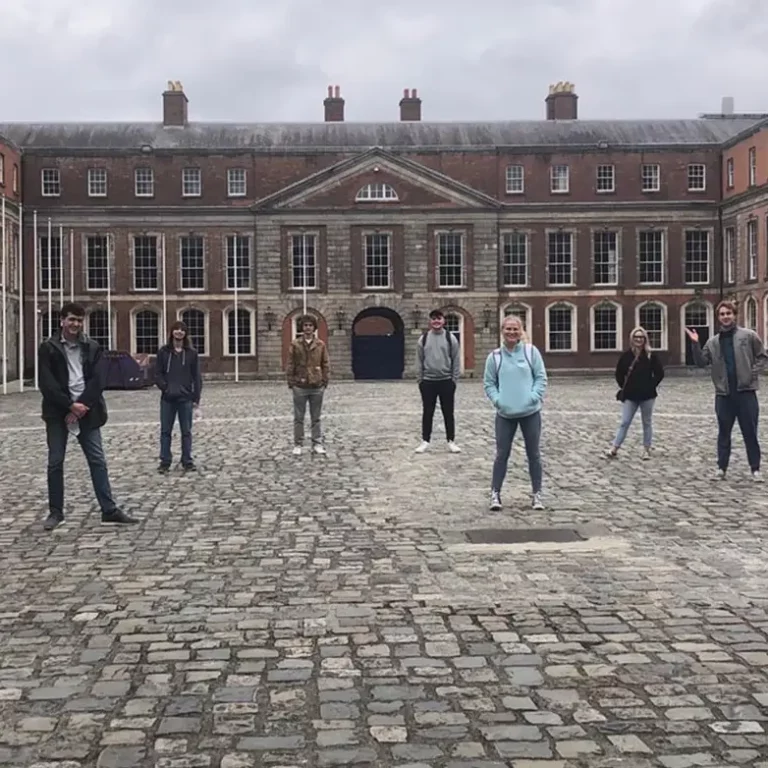 Group of people standing in front of a historic brick building with cloudy sky backdrop.