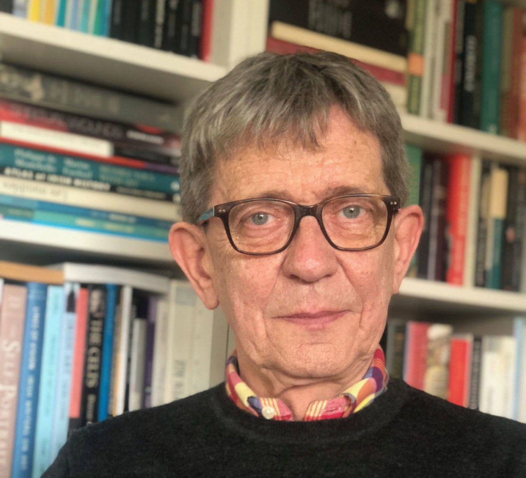 Man wearing glasses in front of a bookshelf filled with colorful books.