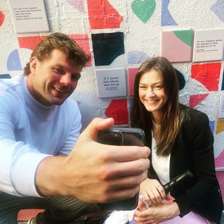 Smiling friends taking a selfie in front of a colorful wall with quotes.