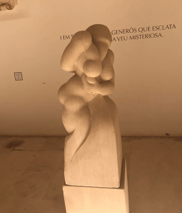 Abstract stone sculpture against a wall with mysterious text, showcasing organic shapes and curves.