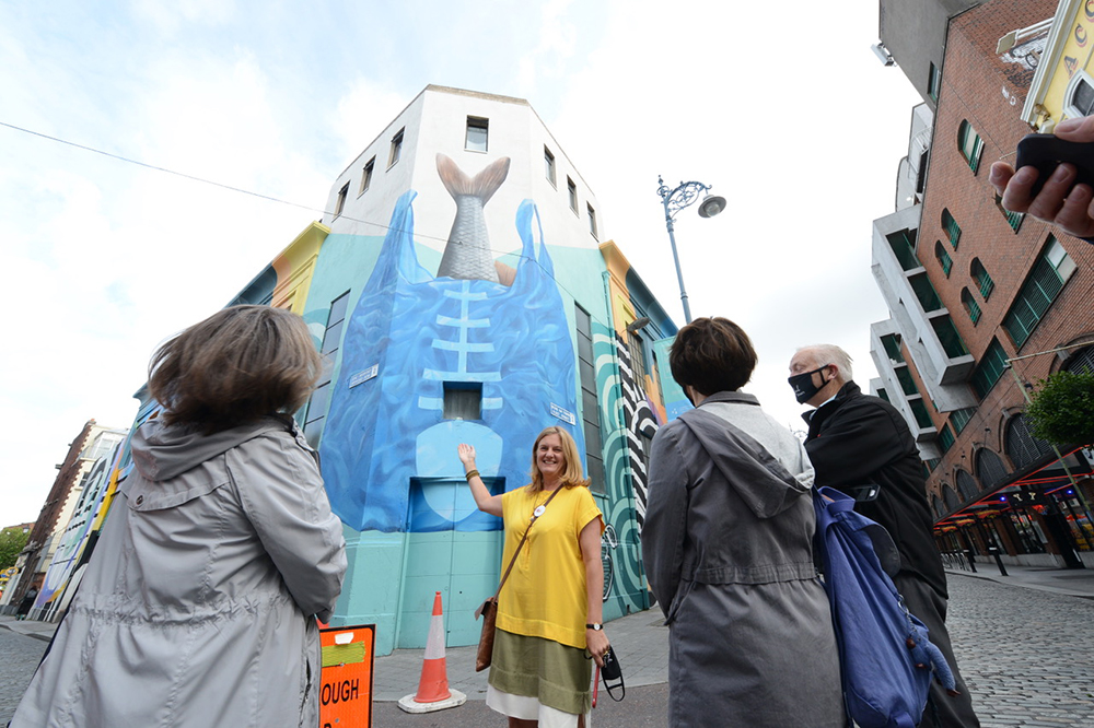 Group admiring vibrant whale mural on urban building wall during a street art tour.