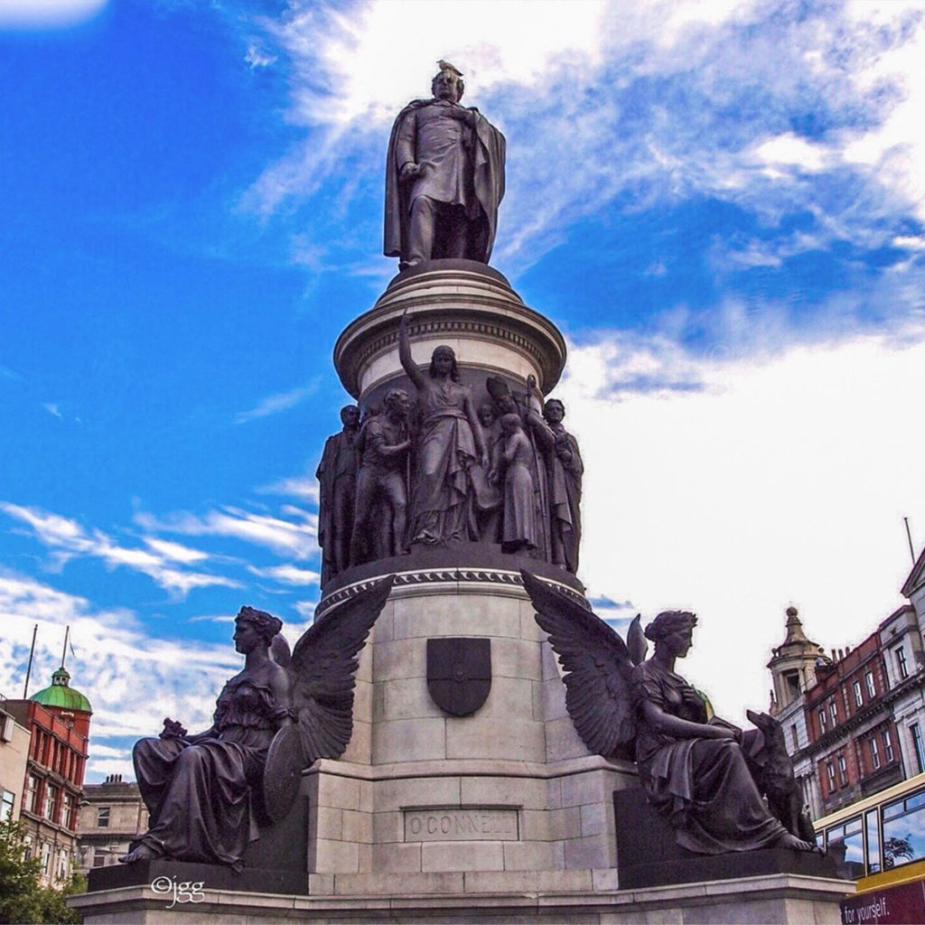 O'Connell Monument in Dublin, Ireland, against a bright blue sky, featuring detailed statues and architectural design.