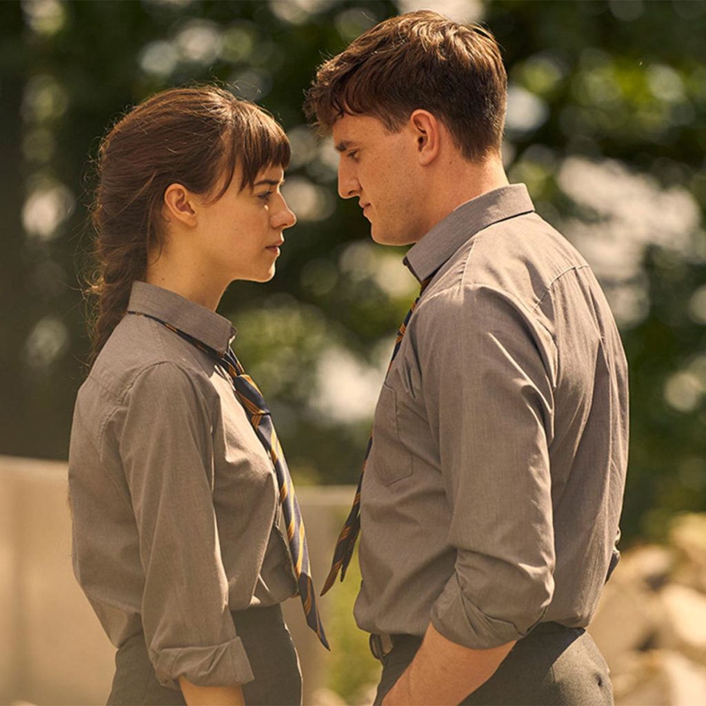 A young couple in school uniforms stand closely facing each other outdoors, creating an intimate and emotional atmosphere.