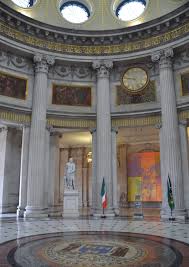 Stately interior of domed building with columns, marble floor, statues, and flags, showcasing grand architectural design.