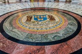 Intricate marble floor medallion with shield design and figures in a grand building.