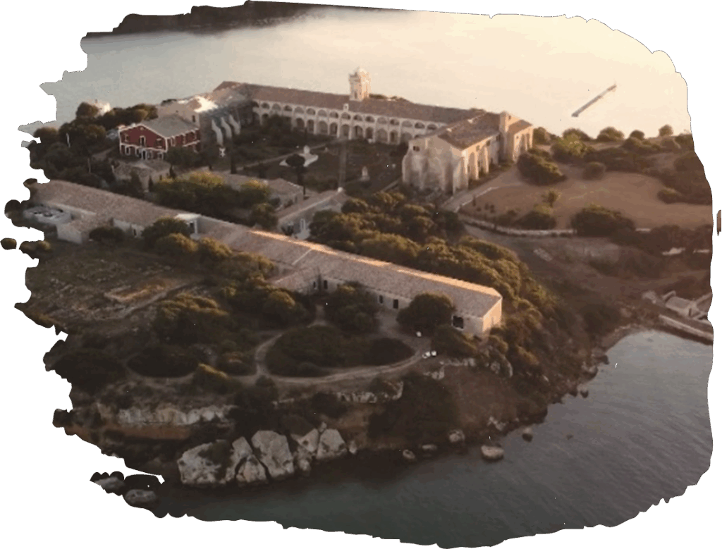 Aerial view of a historic coastal monastery surrounded by water, showcasing architecture and scenic landscapes at sunset.