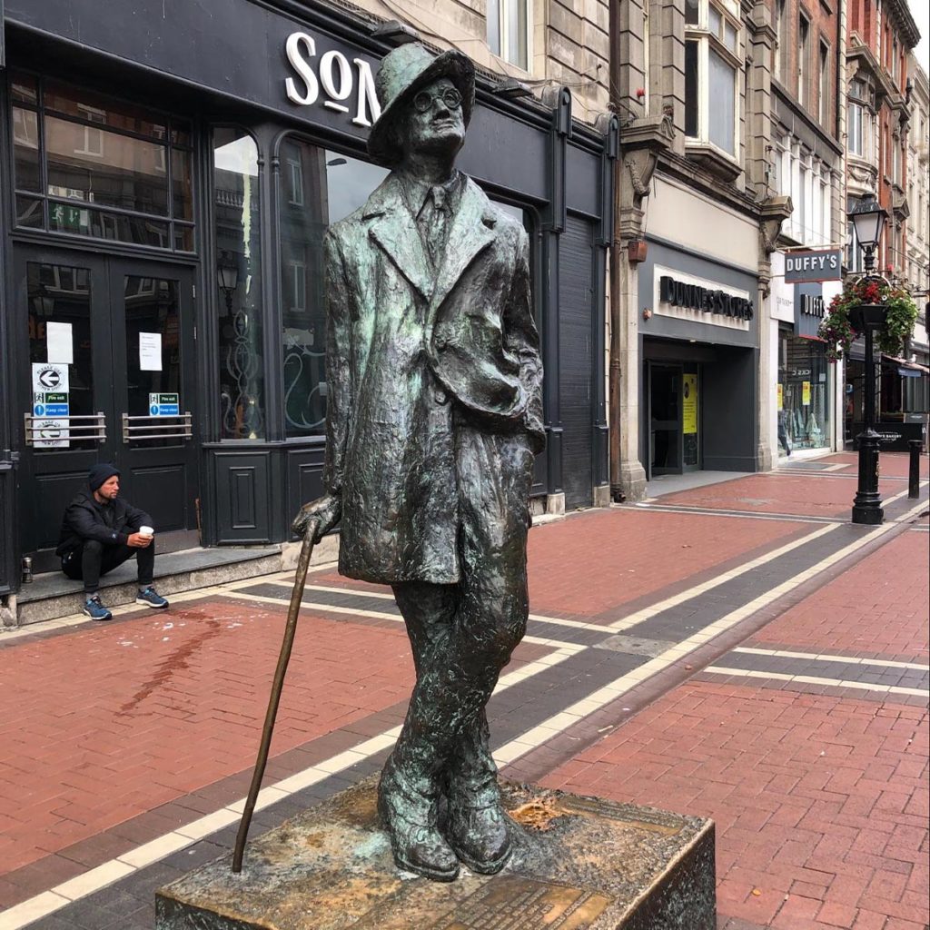 Statue of a man with a cane outside shops on a city street.