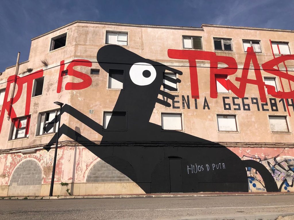 Street art mural on building façade with bold red text and black abstract creature.