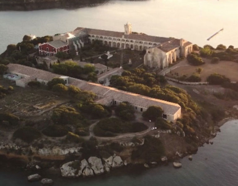 Aerial view of historic island monastery surrounded by water and lush greenery at sunset.