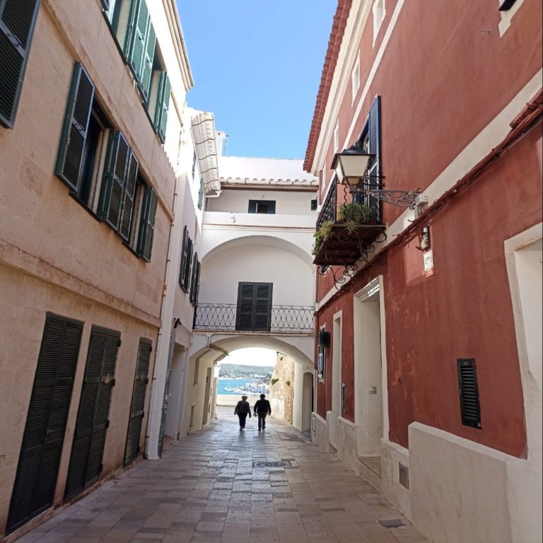 Narrow alley with colorful buildings leading to a scenic coastal view under a clear blue sky.