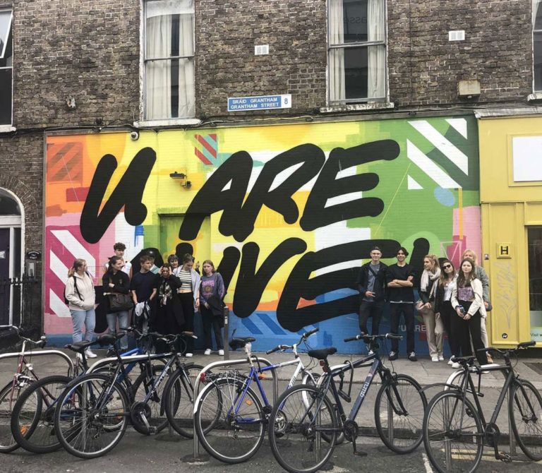 Street art mural with vibrant colors and You Are Alive text, people and bicycles in front.