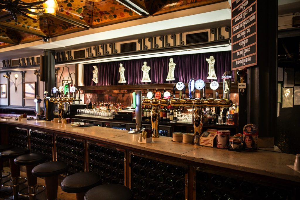 Elegant pub interior with bar stools, draft beer taps, and decorative statues, capturing a cozy and inviting atmosphere.