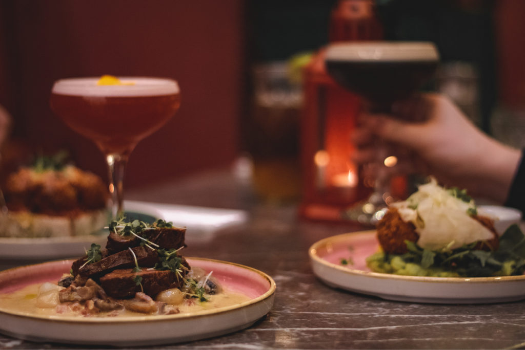 Elegant dining scene with gourmet dishes and cocktails on a stylish table setting.