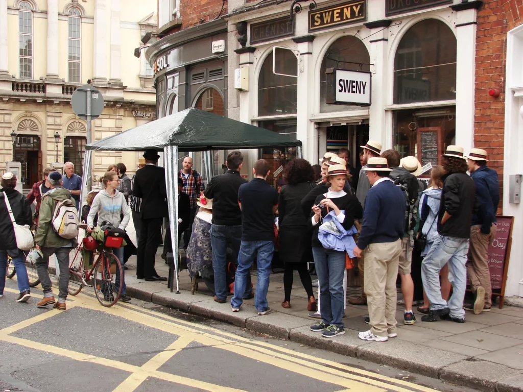 People gathered outside Sweny's Pharmacy, Dublin, wearing hats and chatting, showcasing historic charm.