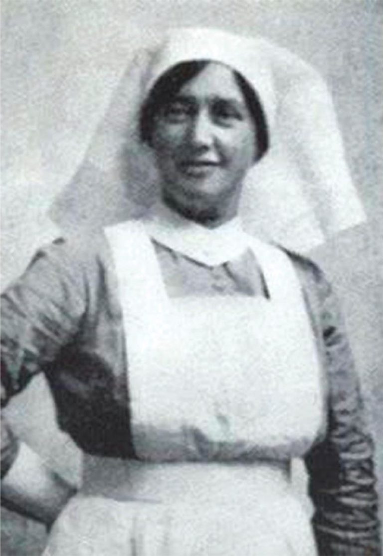 Black and white photo of a historical nurse in traditional uniform, wearing a white apron and head covering.