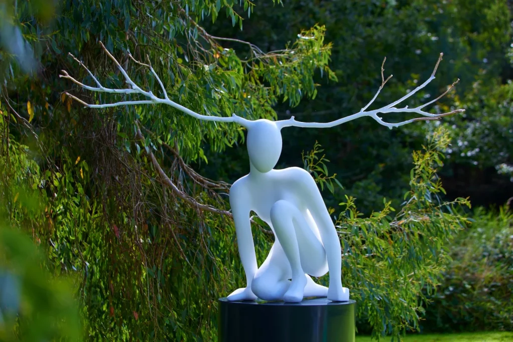 White abstract sculpture with antler-like branches in a green garden setting.