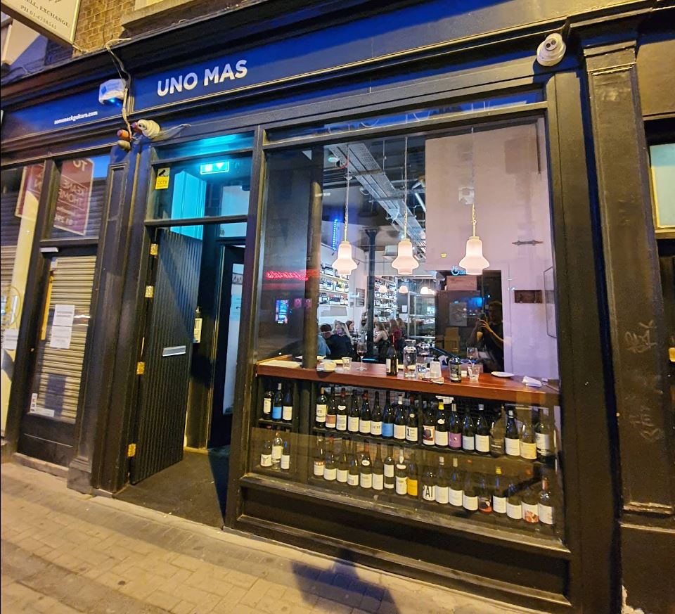 Exterior view of Uno Mas restaurant showcasing its inviting ambiance and wine display through the window.